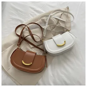 Detail of brown and white saddle bags with gold metal clasps on a beige blazer