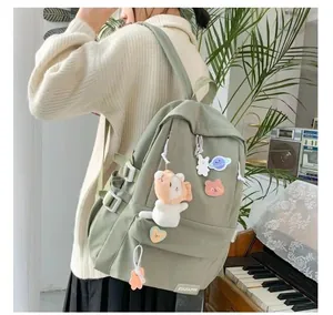 Detalle de una mochila escolar verde claro con pines lindos y colgante de peluche de gato