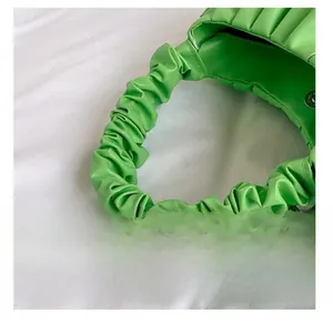 Detailed close-up of the ruched handle and green pleated texture on a soft baguette bag