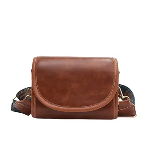 Sac bandoulière en cuir marron avec surpiqûres blanches et large sangle tissée style ethnique