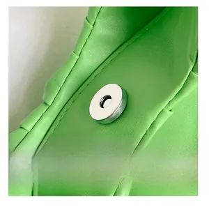 Close-up of silver magnetic metal clasp and green pleated PU leather bag texture