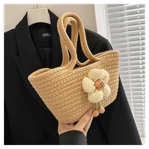 Detail einer handgewebten beigen Strohhandtasche mit großer Stoffblume und Kugelanhängern