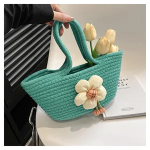 Detail einer minzgrünen geflochtenen Handtasche mit einer cremeweißen dekorativen 3D-Blume