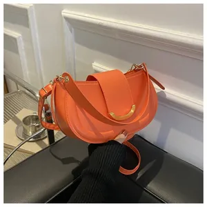 Close-up of bright orange saddle bag with gold metal buckle and smooth stitching details