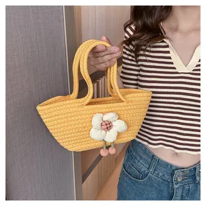 Detail der gelben geflochtenen Handtasche mit weißen 3D-Blumen und rosa Pompons
