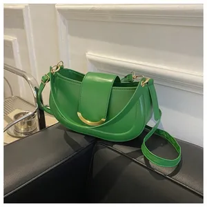 Detail of emerald green saddle bag with elegant gold crescent clasp and leather texture