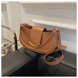 Brown saddle bag with gold metal buckle detail on a black leather sofa background