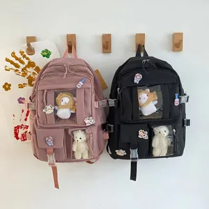 Dettaglio di zaini scolastici in nylon rosa e nero con simpatici peluche e badge