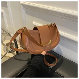 Detail of a brown leather saddle bag featuring a stylish gold crescent metal buckle