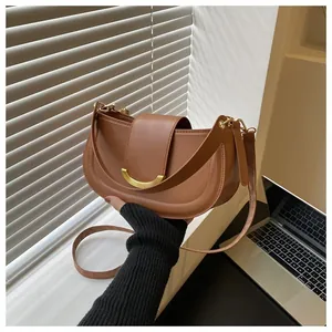 Detail of a brown leather crescent saddle bag with gold hardware on a desk with a laptop