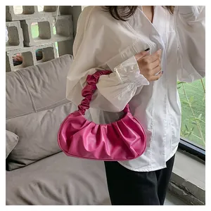 Close-up of vibrant magenta pleated cloud bag held by a model in a minimalist setting