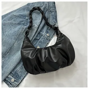 Detail of black ruched crescent bag with woven handle on blue denim backdrop