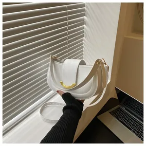 White saddle bag with gold metal trim and leather strap shown in natural light