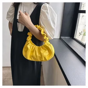 Detail of a bright yellow pleated cloud bag carried by a model in a stylish outfit