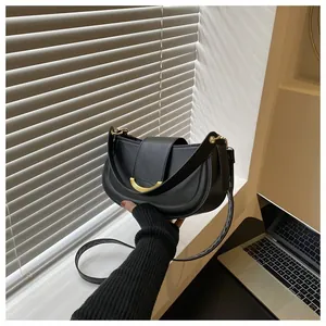 Detail of black saddle bag featuring golden crescent metal clasp and dual shoulder straps