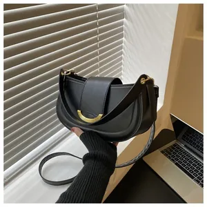 Detail of black saddle bag featuring golden crescent buckle and smooth faux leather finish