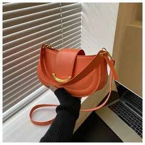 Detail view of bright orange saddle bag featuring golden hardware in urban hand-held scene