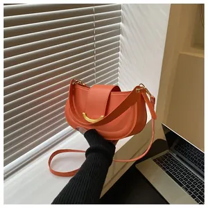 Detail of orange saddle bag showing smooth PU leather and gold crescent metal buckle