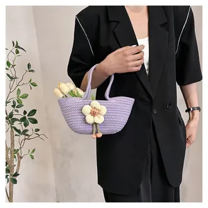 Detailansicht einer lila gewebten Handtasche mit gelber Blume und rosa Anhänger