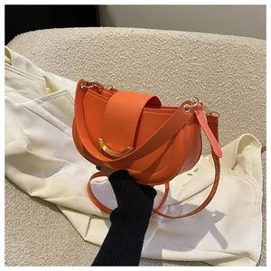 Detailed view of the orange saddle bag featuring a gold crescent buckle and leather strap