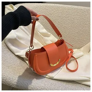 Macro shot of orange leather saddle bag with gold buckle and adjustable shoulder strap