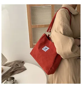 Detail view of red corduroy tote bag with silver metal rings and leaf pattern label
