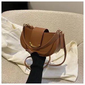 Detailed close-up of a caramel brown leather saddle bag with gold crescent metal hardware
