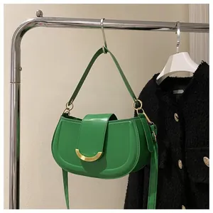 Detailed close-up of a green saddle bag with a golden crescent buckle on a metal hanger