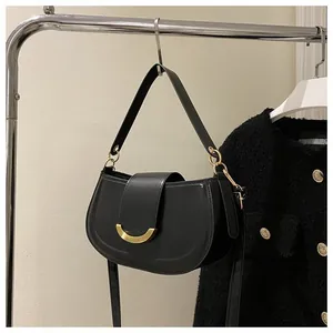 Detail of black saddle bag with gold crescent buckle on a silver hanger with tweed jacket