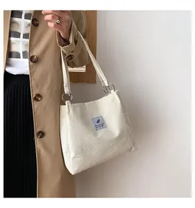 Close-up of white corduroy tote bag with silver ring shoulder strap and gray textile patch