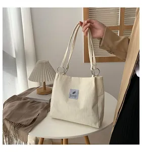 Detail of cream corduroy tote bag with blue label on white table with lifestyle props