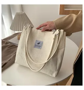 Macro detail of creamy white corduroy tote bag showing metal rings and fabric label