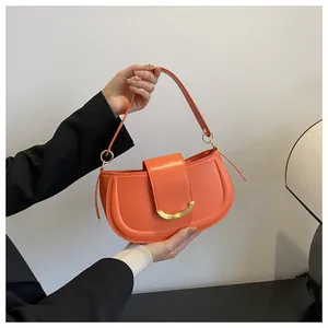 Detail of a bright orange saddle bag featuring a matte leather finish and gold arc hardware