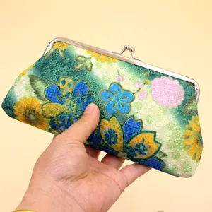 Détail macro de broderie florale vintage sur pochette en tissu avec fermoir bisou
