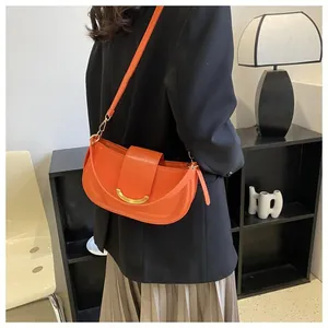 Detail of bright orange saddle bag with gold metal hardware on model in black suit