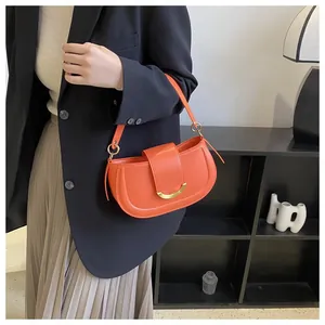 Close-up of vibrant orange saddle bag with gold crescent buckle on a model