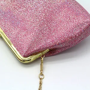 Detail van roze glitter damesclutch met gouden metalen frame en fijne kettingriem