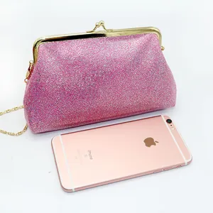 Roze glitter avondtasje met gouden metalen gesp en ketting naast een mobiele telefoon maat