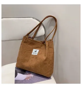 Detail of brown corduroy tote bag showing vertical stripe texture and white logo patch