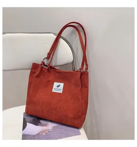 Detailed texture of orange corduroy tote bag with metal ring and white woven label