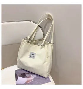 Detailed texture of cream white corduroy tote bag with black feather label on white chair