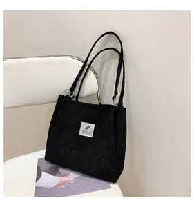 Detail of black corduroy tote bag with white woven label on a minimalist white chair