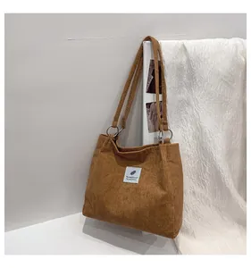 Detail of caramel corduroy tote bag with metallic rings and embroidered logo patch