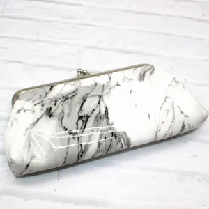 Detail of white marble pattern clutch with silver kiss-lock clasp on a brick background