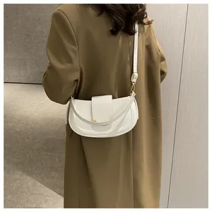Detailed view of a white crescent saddle bag with gold hardware on a trench coat