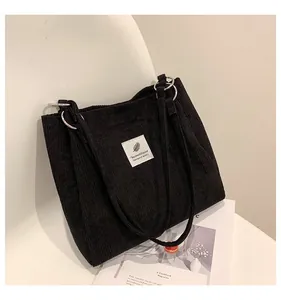 Detail view of black corduroy tote bag showing metal ring and white fabric label