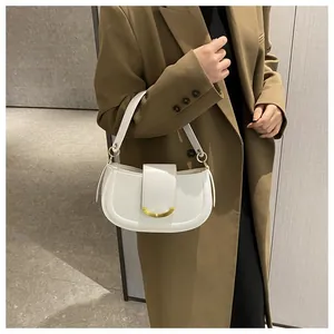 On-shoulder view of a sleek white saddle bag with a metallic gold semicircular buckle