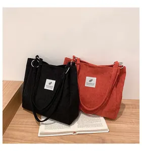 Detailed texture of black and orange corduroy tote bags on a wooden table with a book