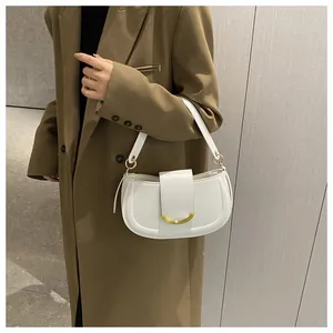 Close-up of white leather saddle bag with golden metal buckle on woman in brown blazer