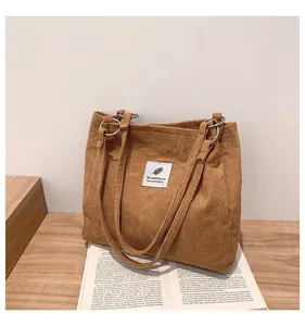 Detail of corduroy tote bag in brown with metal rings and decorative logo patch